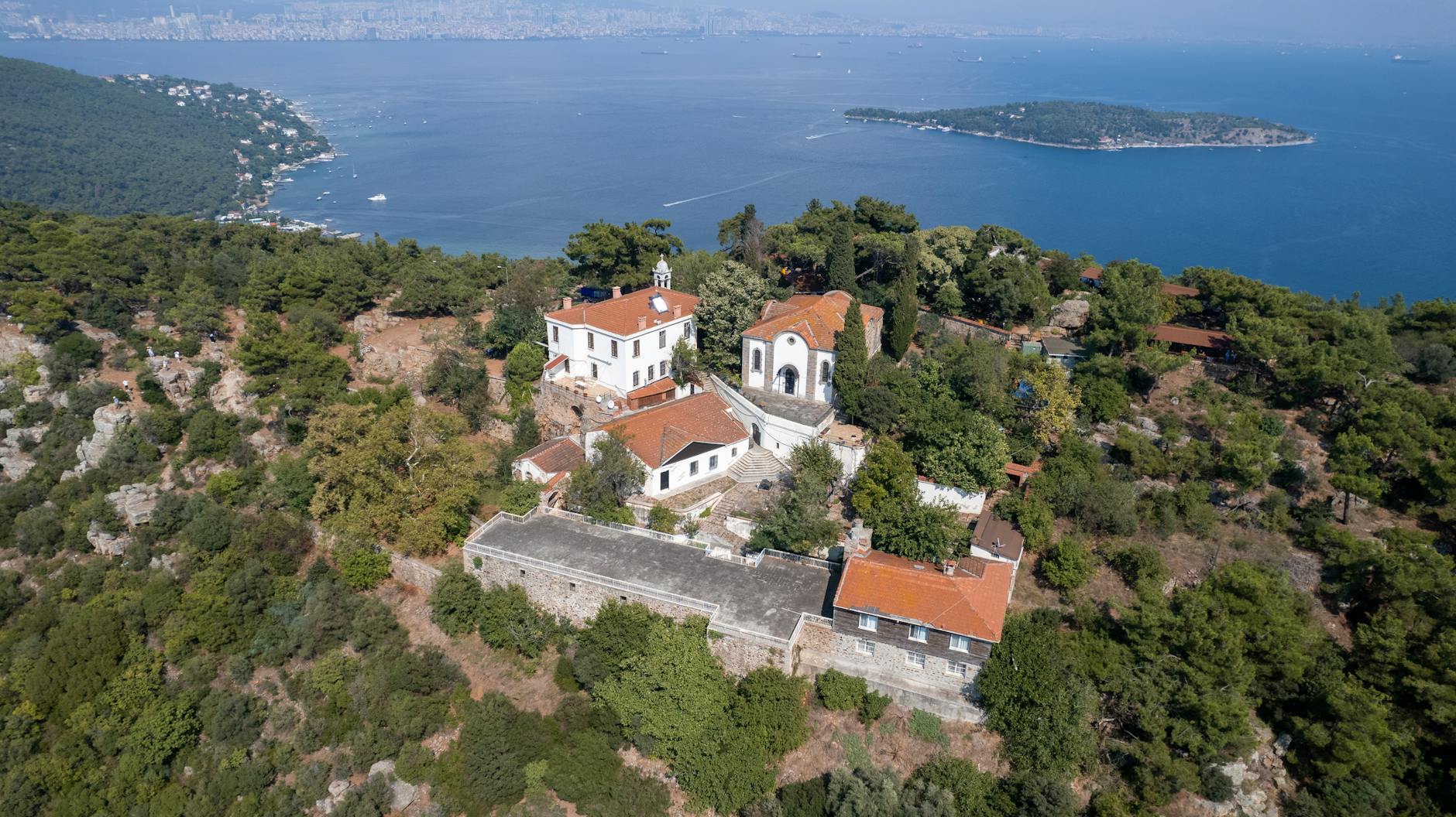 Aerial view of a historic white monastery complex on a forested island hill.