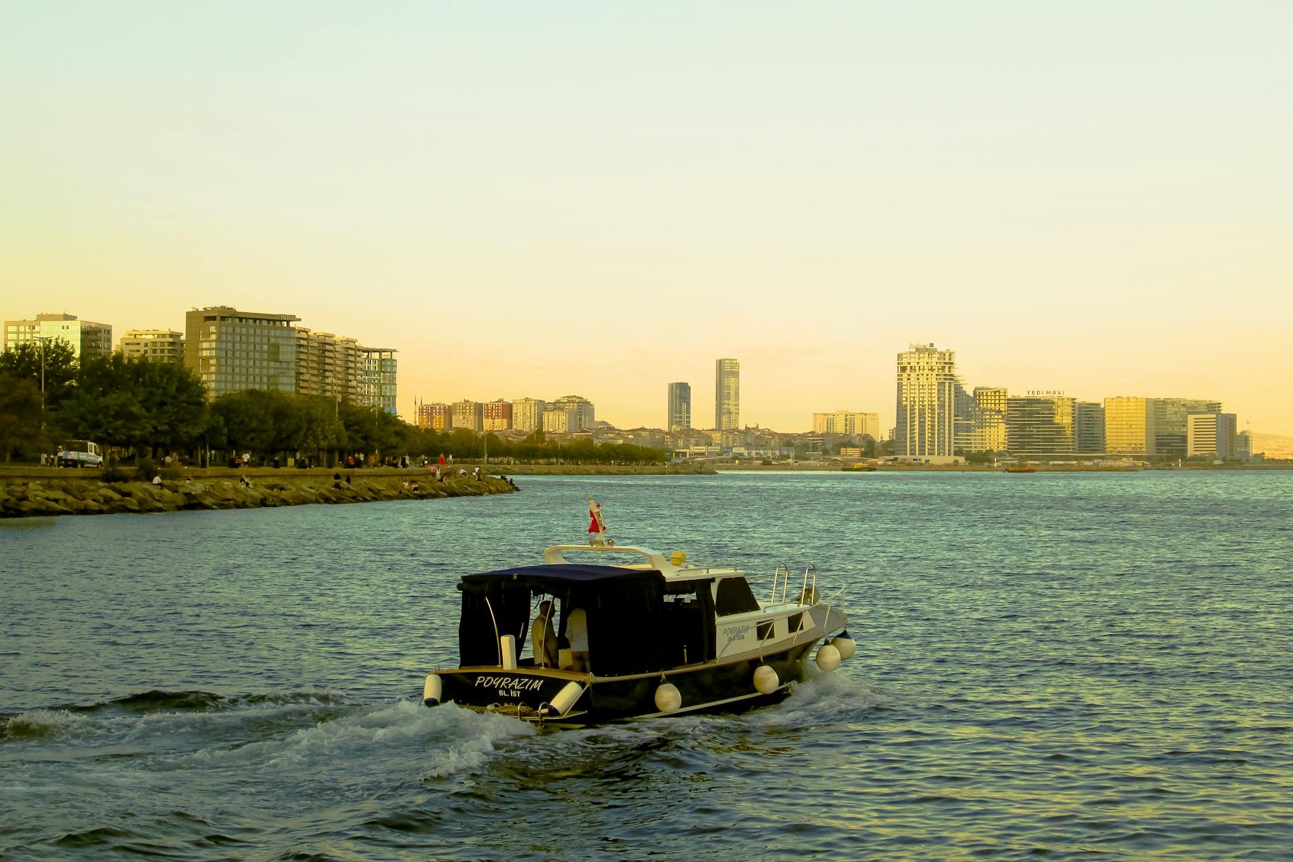 A motorboat cruises along the Bakirkoy waterfront with modern residential skyscrapers in the distance.