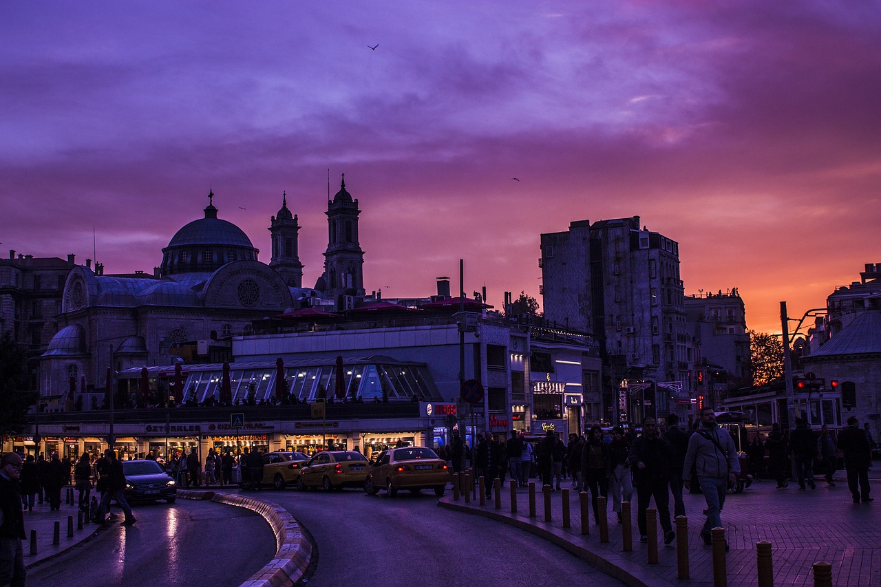 People and taxis move through a Beyoglu street under a vibrant purple sunset sky.