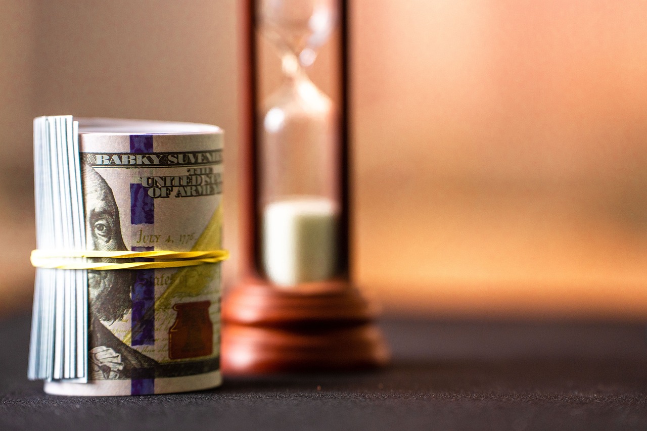 A roll of US dollar bills sits beside an hourglass representing changing exchange rates.