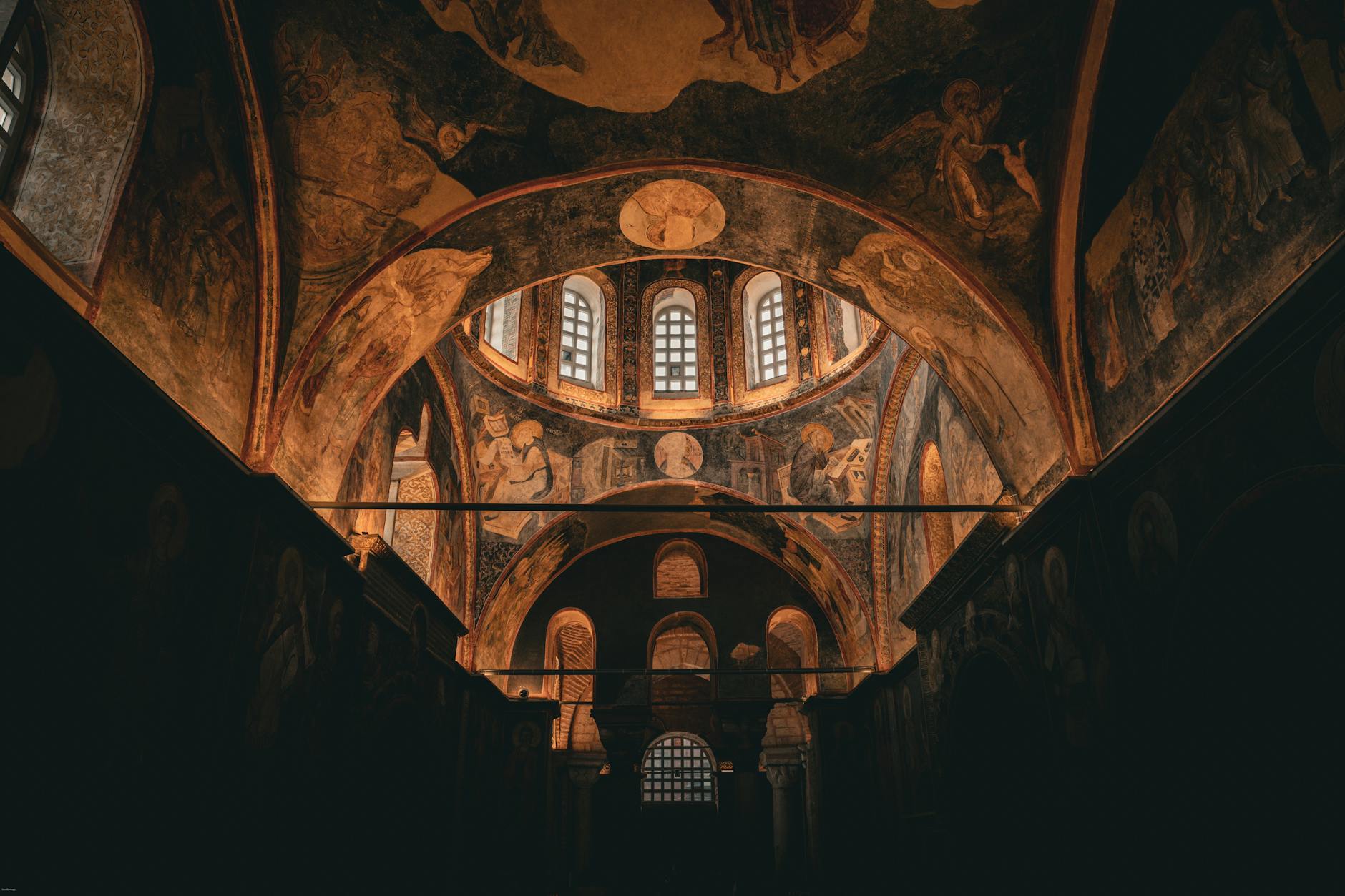 Dark, atmospheric interior view showing the richly painted Byzantine frescoes and mosaics on the dome and arches of the Kariye Mosque (Chora Church) in Istanbul.