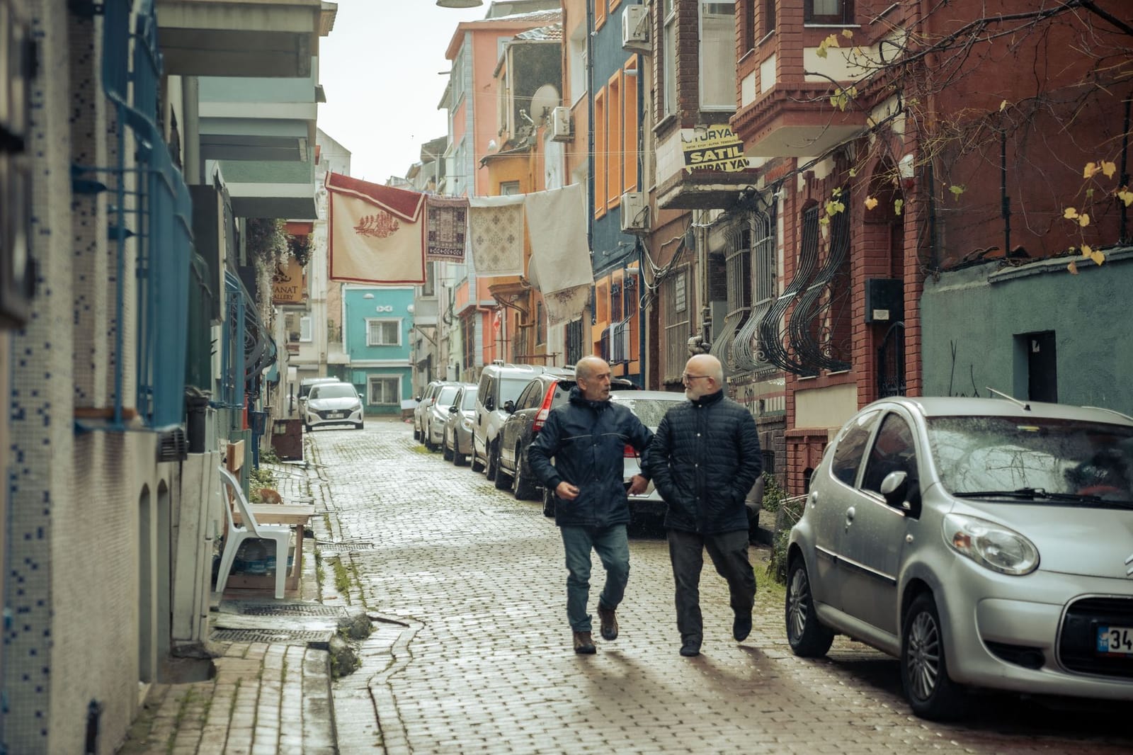 Two men walking along a quiet cobblestone alley with laundry hanging overhead.