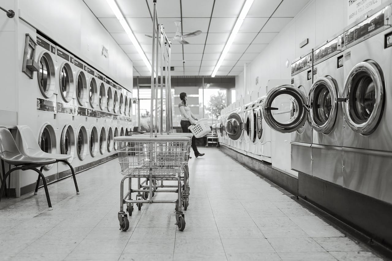 A bright laundromat aisle filled with rows of commercial washers and laundry carts.