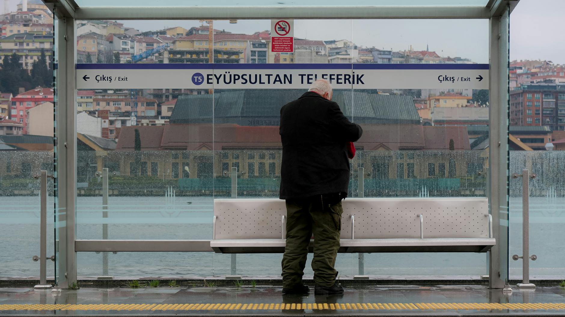 A man stands at the Eyüpsultan Teleferik station platform overlooking the Golden Horn.