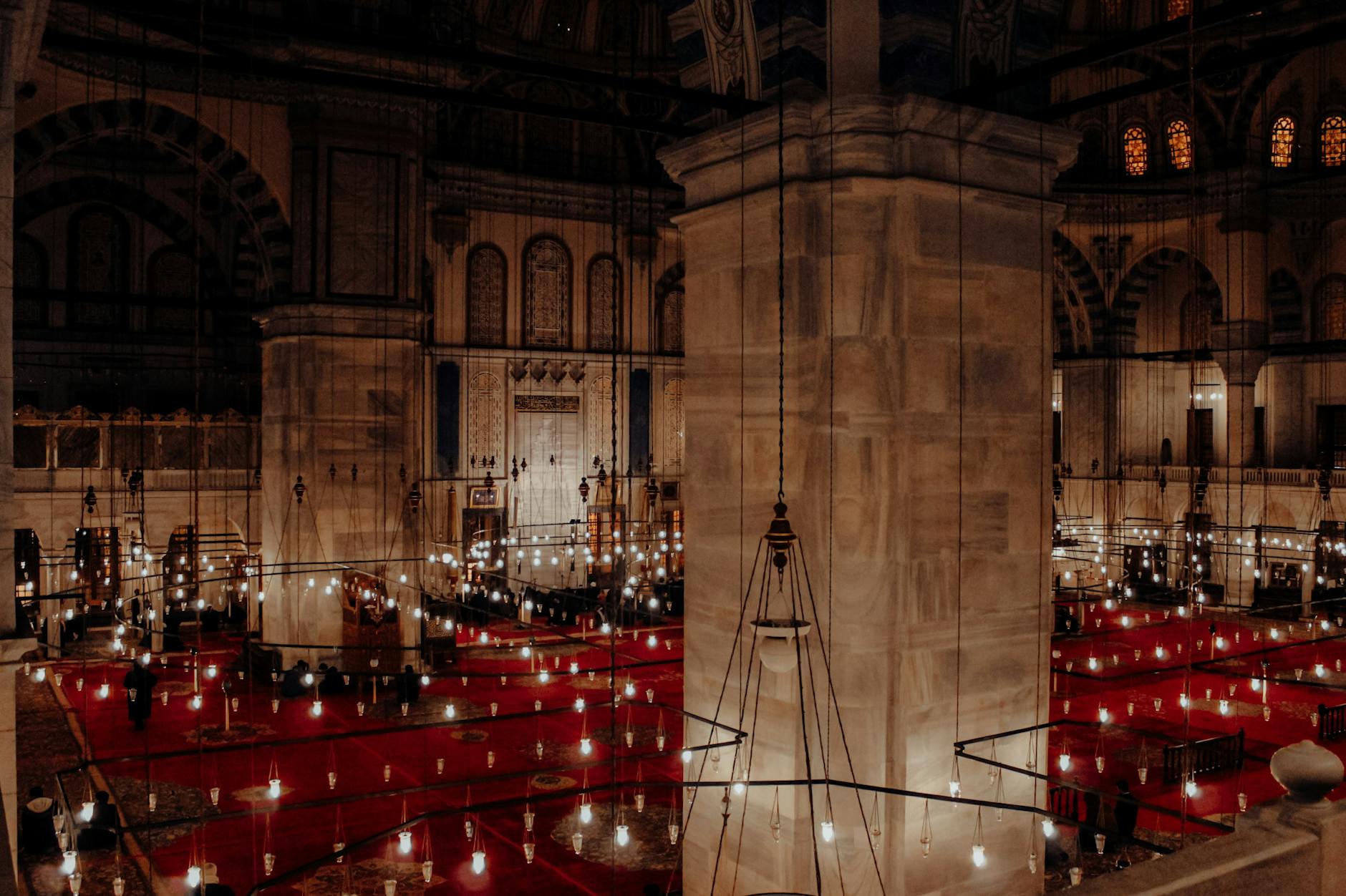 Interior view of Fatih Mosque with rows of hanging lamps and carpets.