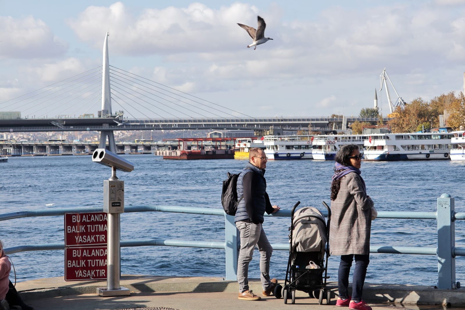 A family with a baby stroller pauses along the wide, flat waterfront promenade in Istanbul.