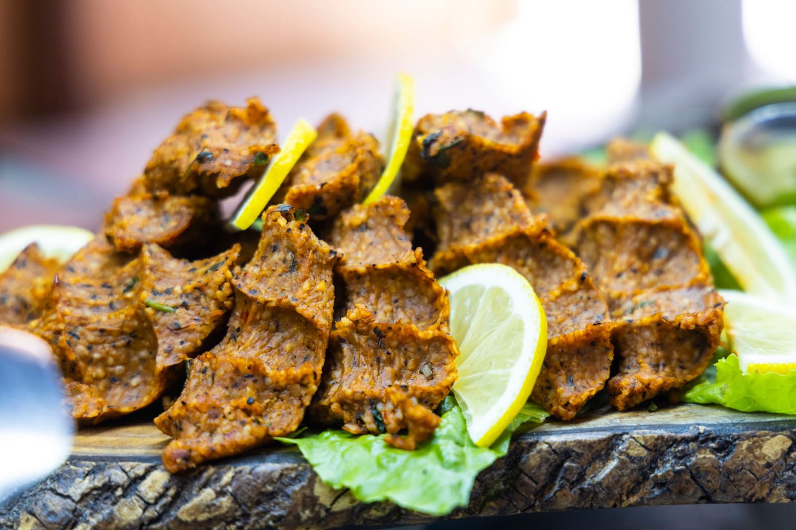 A wooden serving board filled with hand-molded spicy cig kofte and fresh lemon slices.