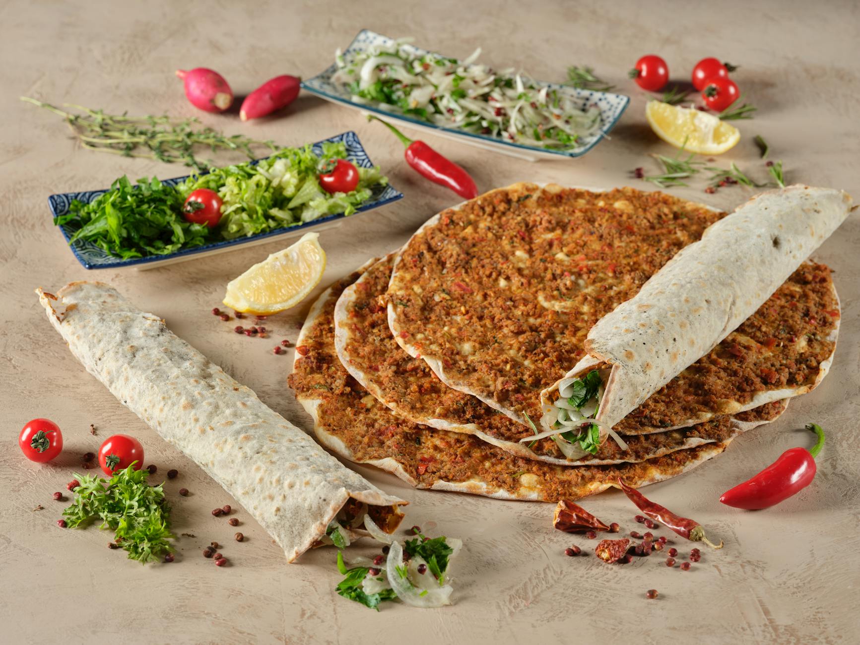 An artistic arrangement of multiple thin crust lahmacun, some rolled with fresh salad inside.