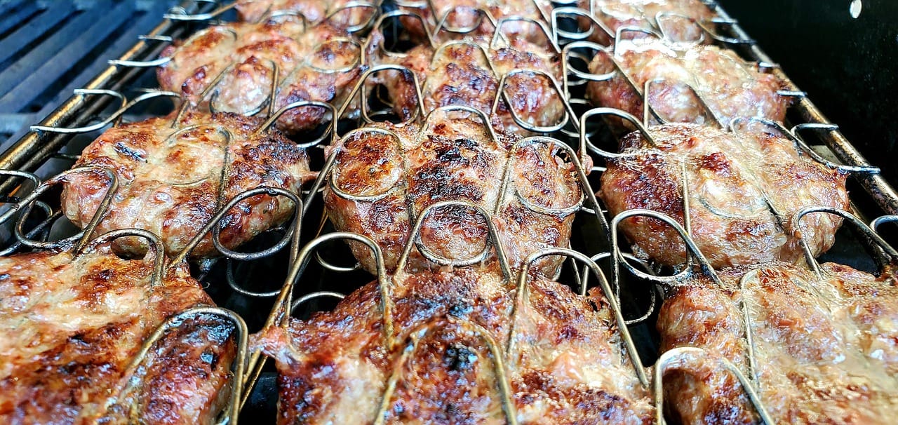 Traditional Turkish kofte meatballs sizzling on a metal grill rack.