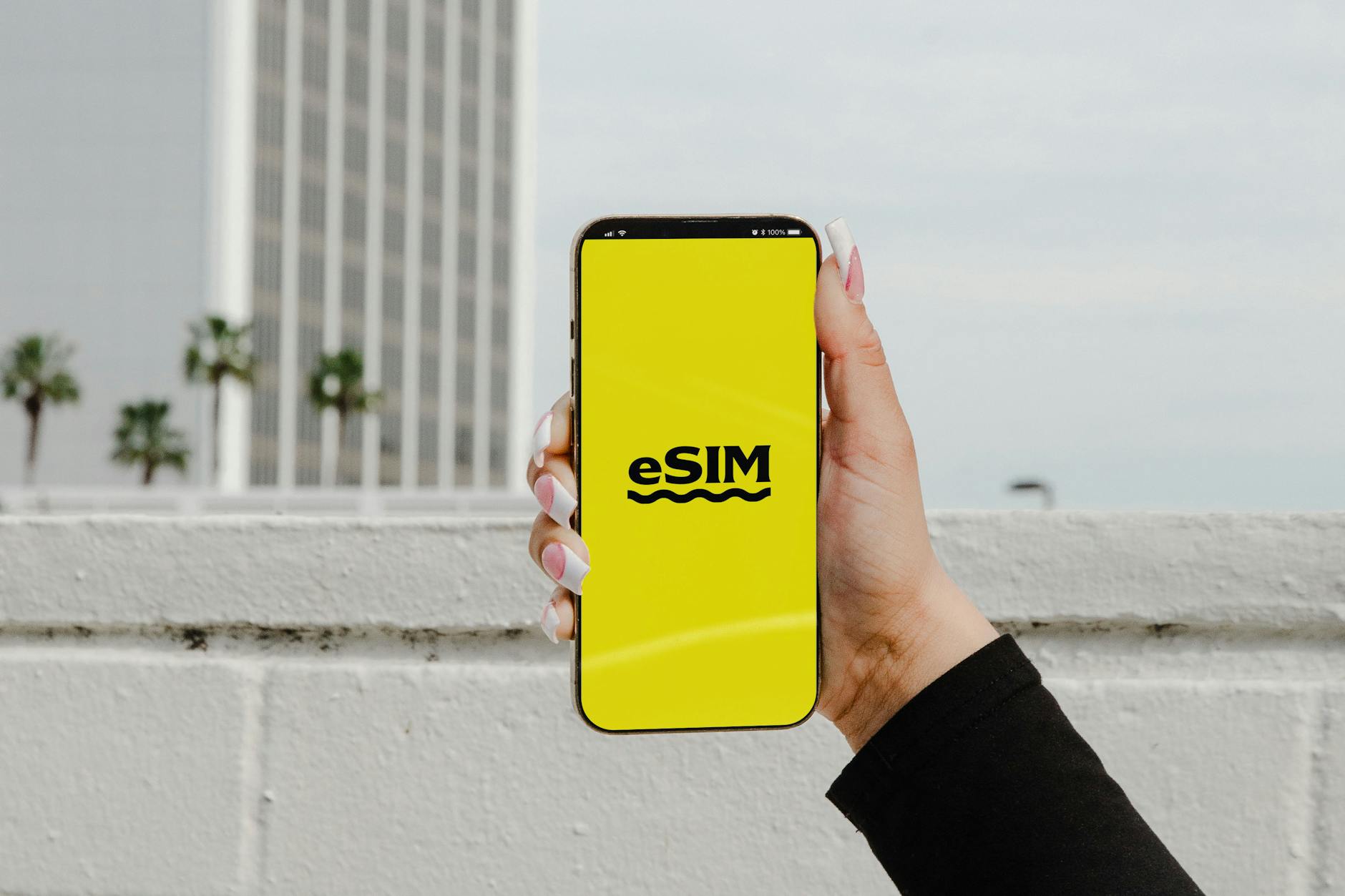 A hand holds a smartphone displaying a bright yellow eSIM logo screen.