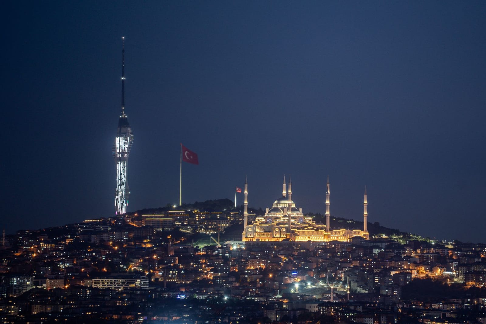 Illuminated Camlica Tower and Camlica Mosque shine over Istanbul at night.