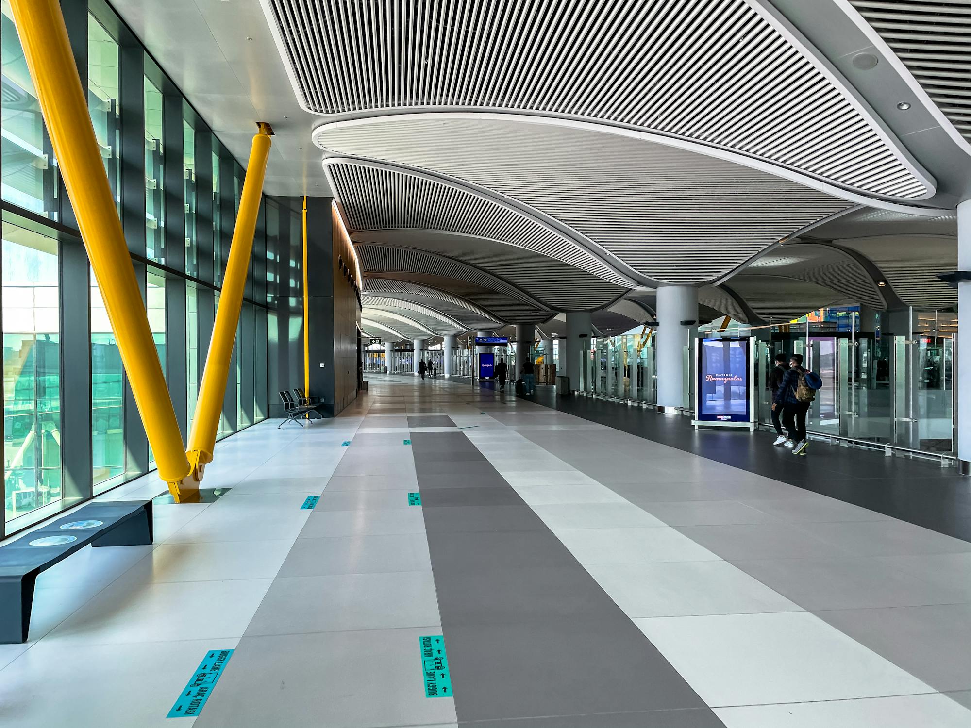 The modern glass and steel interior of Istanbul Airport arrivals hall with passengers and luggage trolleys.