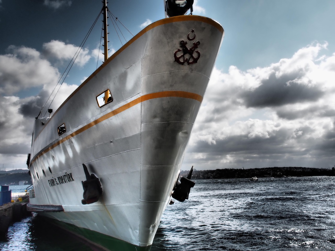 The bow of a classic Turkish ferry vessel navigates the Bosphorus strait under cloudy skies.