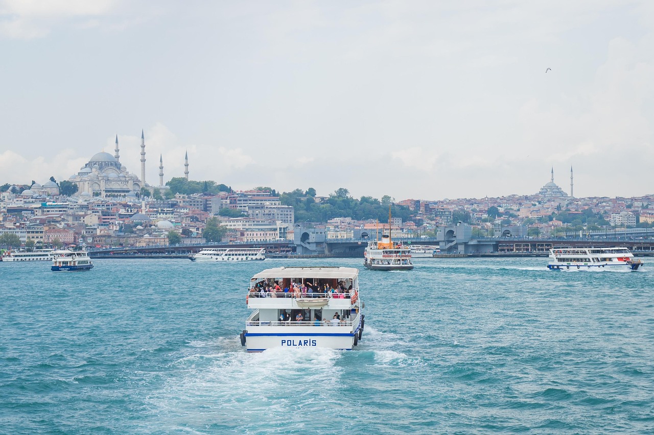 A scenic view across the churning blue waters of the Golden Horn in Istanbul, featuring several ferries including the 'Polaris' in the foreground. In the background, the dense cityscape rises, dominated by Ottoman-era mosques on the skyline, suggesting a break from the major crowds—a perfect alternative when one feels 'I am done with the Sultanahmet crowds so I go to Little Hagia Sophia instead'—to enjoy the maritime life and views toward the historical peninsula.