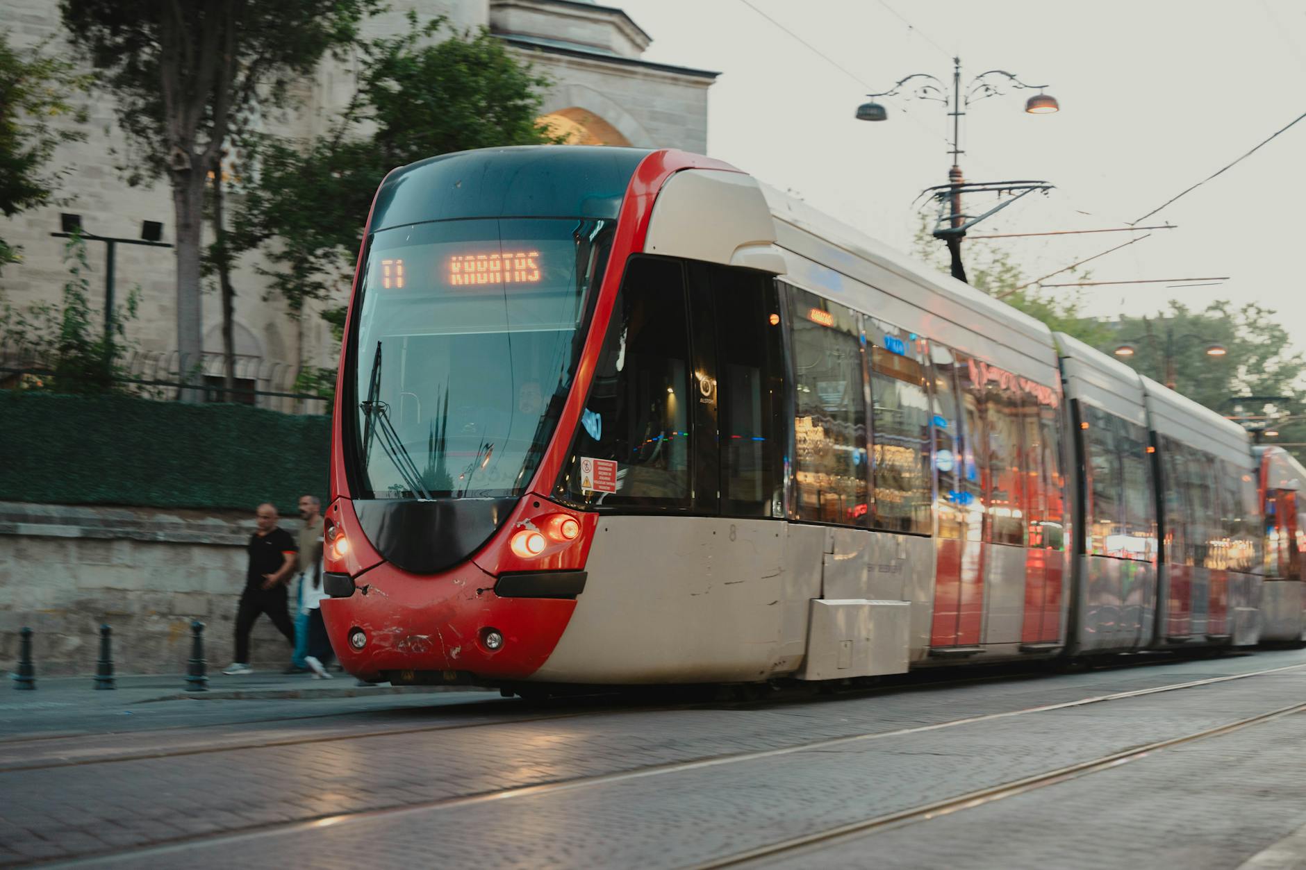 A modern red and white T1 tram navigates through the historic streets of Istanbul's Old City.