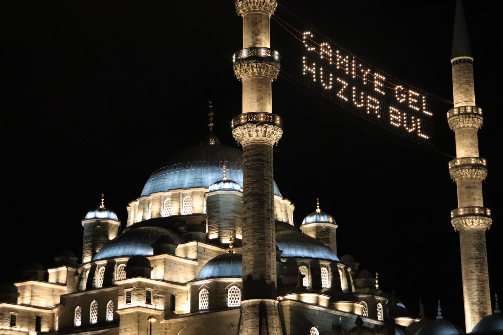 Illuminated mahya message shines between minarets of an Istanbul mosque during Ramadan.