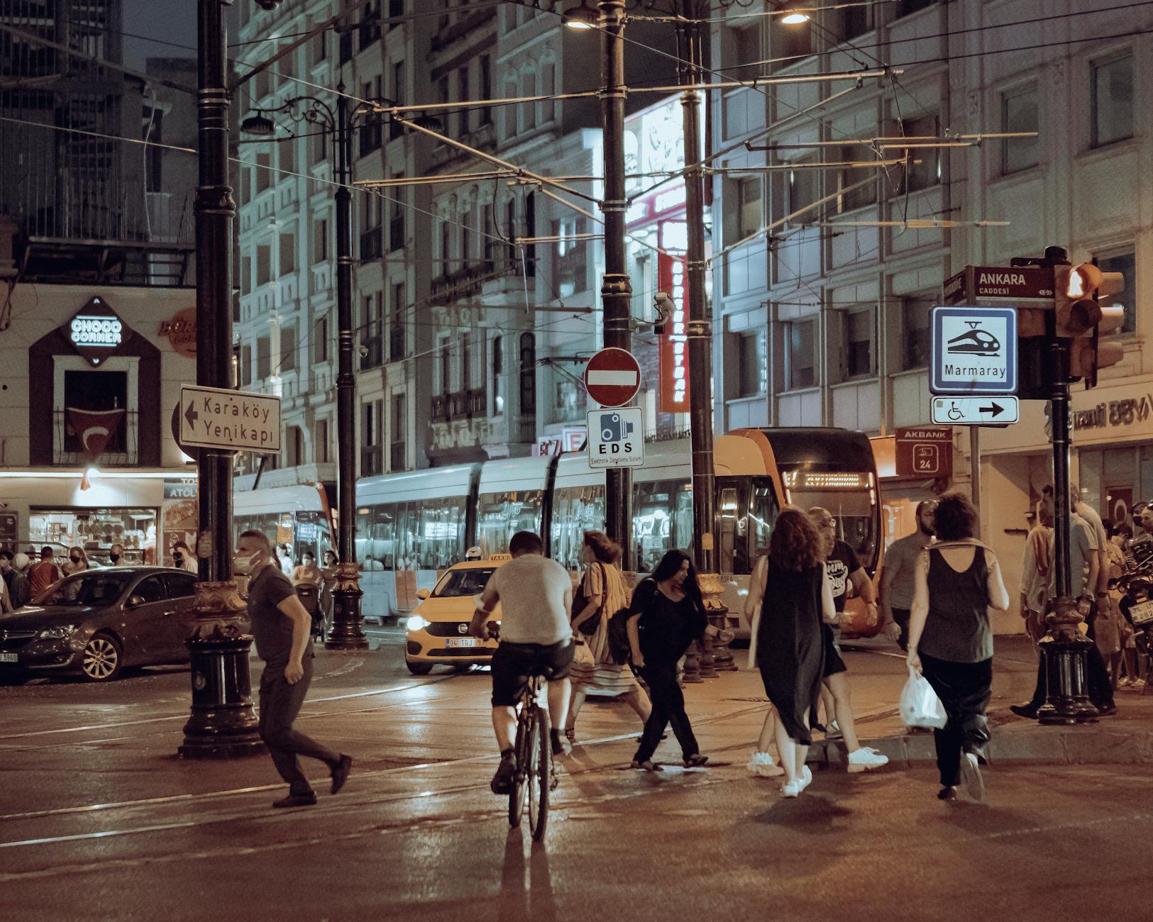A modern tram passes a street sign pointing towards the Yenikapı district at night.