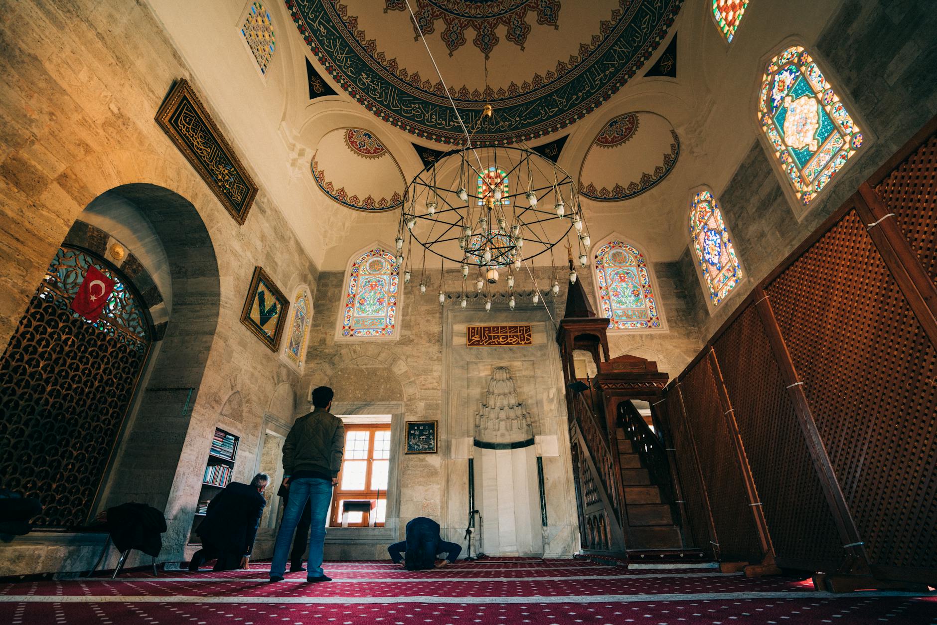 People pray inside the Kilic Ali Pasha Mosque beneath a massive and ornate chandelier.