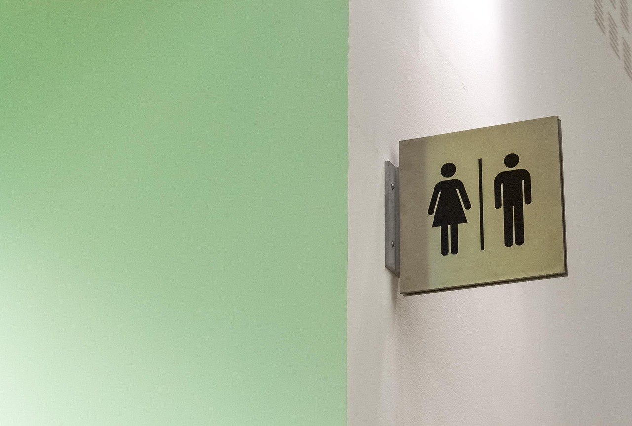 A metal sign with male and female symbols pointing to public restrooms on a clean wall.