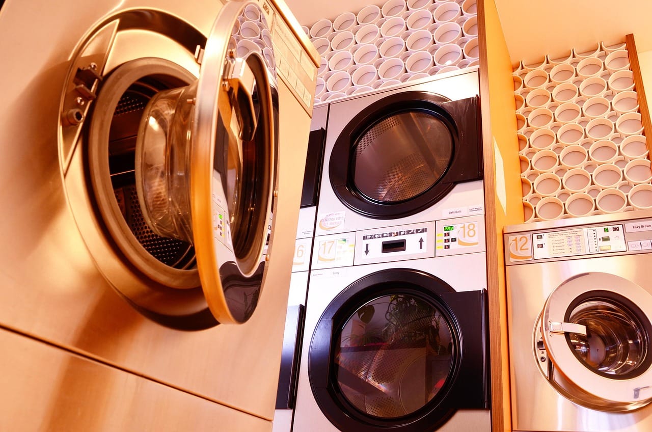 Modern stainless steel coin-operated washing machines and dryers stacked in a laundromat.