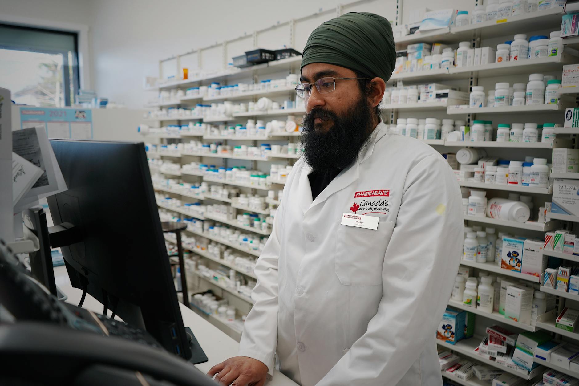 A professional pharmacist with a turban works at a computer station in a pharmacy.