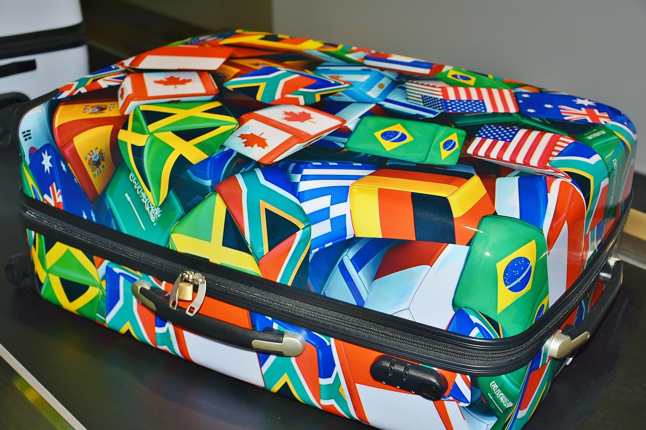 A modern suitcase featuring a colorful design of various international flags on a dark surface.