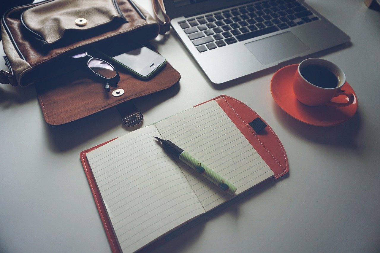 An open notebook and pen placed on a desk next to a coffee cup.