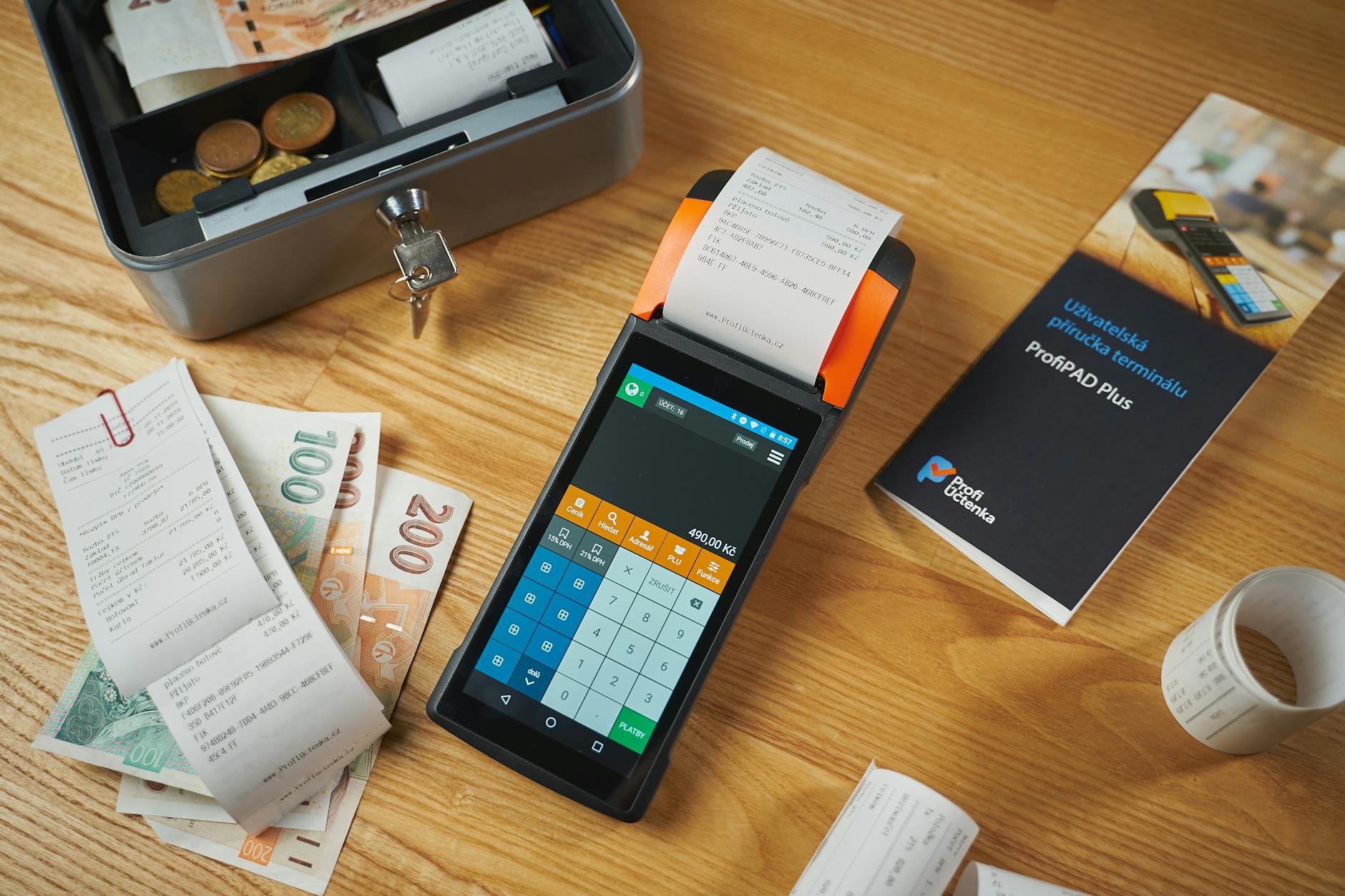 A digital payment terminal surrounded by international cash, coins, and transaction receipts.