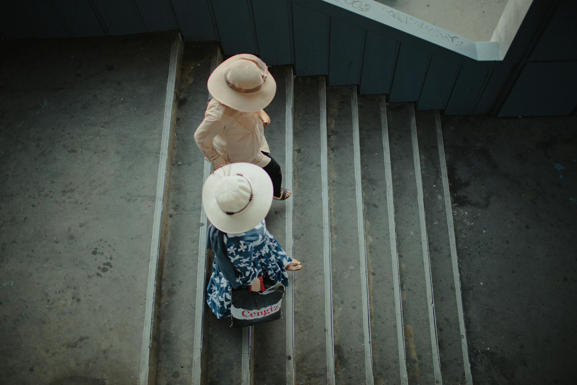 Two women wearing sun hats walk down a set of concrete public transit stairs.