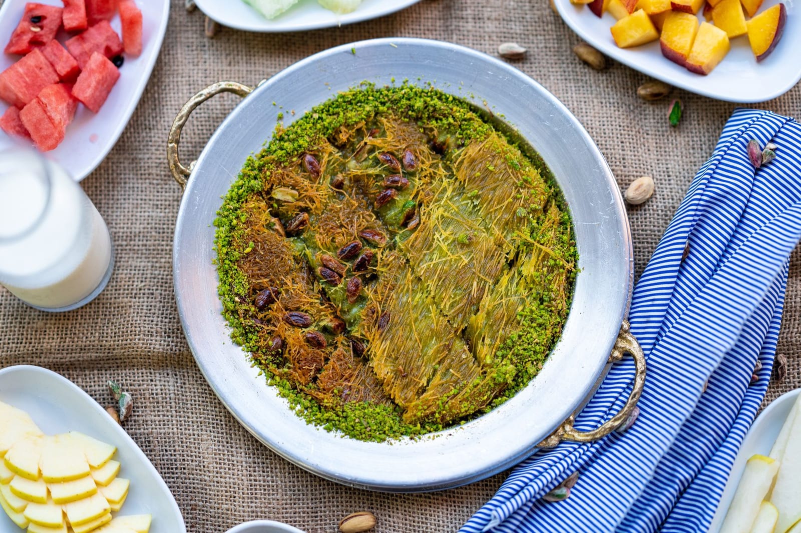 Traditional pistachio hasir kunefe served in a metal pan with fresh fruits.