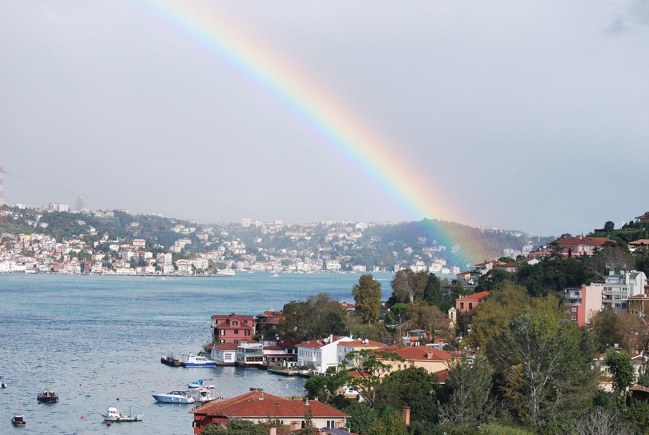 A vibrant rainbow stretches across the sky over traditional waterfront houses along the Bosphorus.