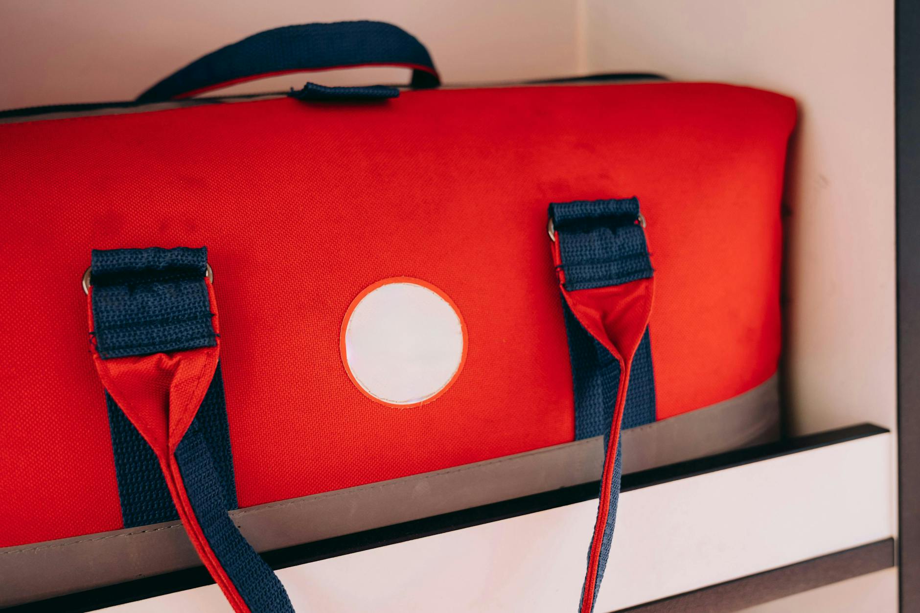 A bright red duffel bag sits inside a white storage locker shelf.