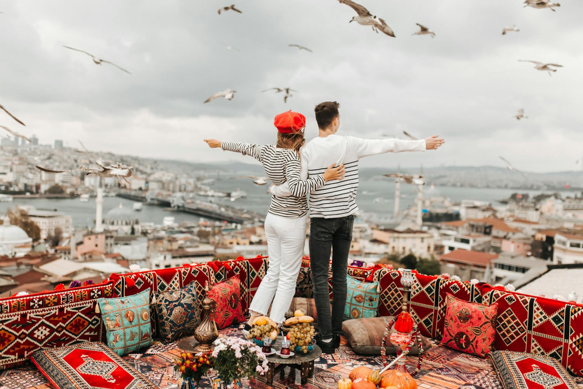 A couple overlooks Istanbul from a decorative rooftop surrounded by flying seagulls.