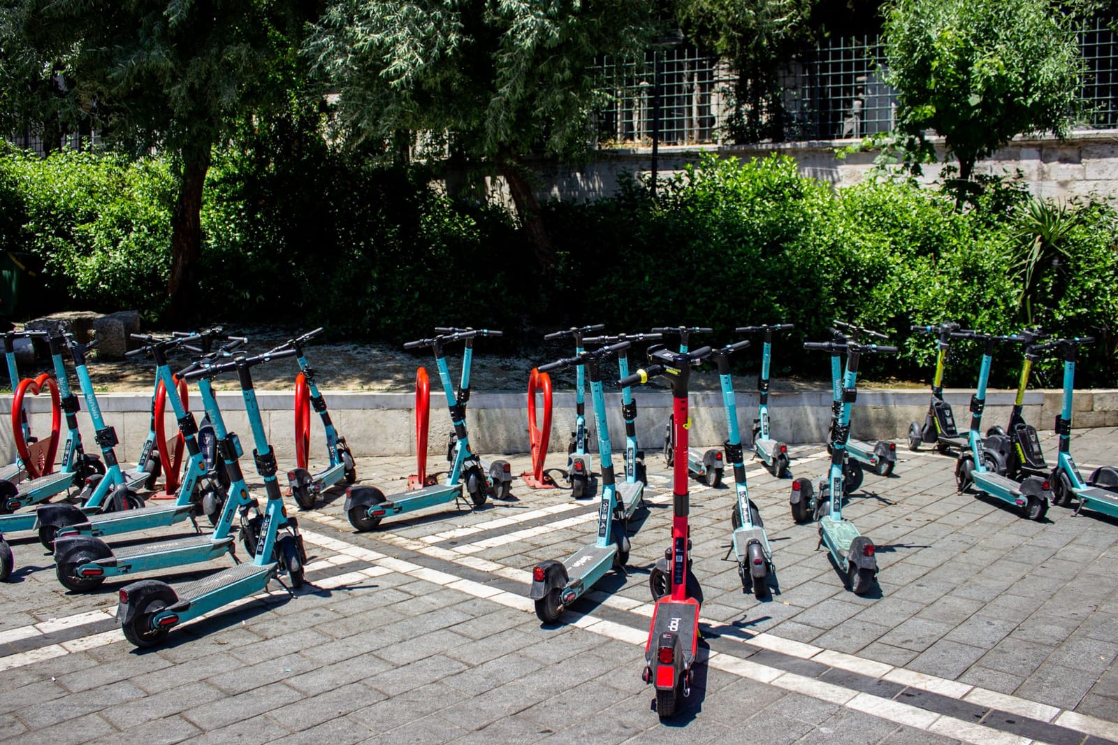 Row of turquoise and red shared electric scooters parked on an Istanbul city square.