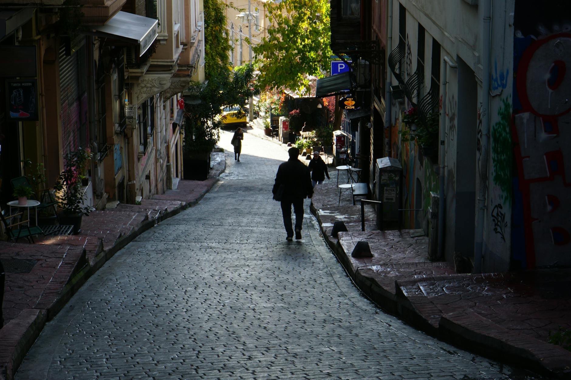 People walk down a narrow cobblestone street in the backstreets.