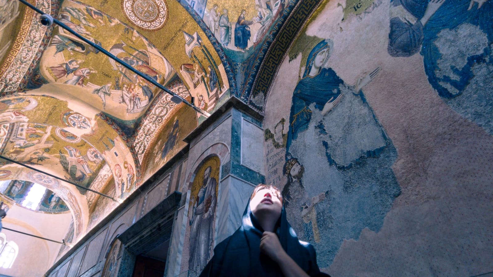 A visitor wearing a head covering admires ancient mosaics inside Chora Mosque.