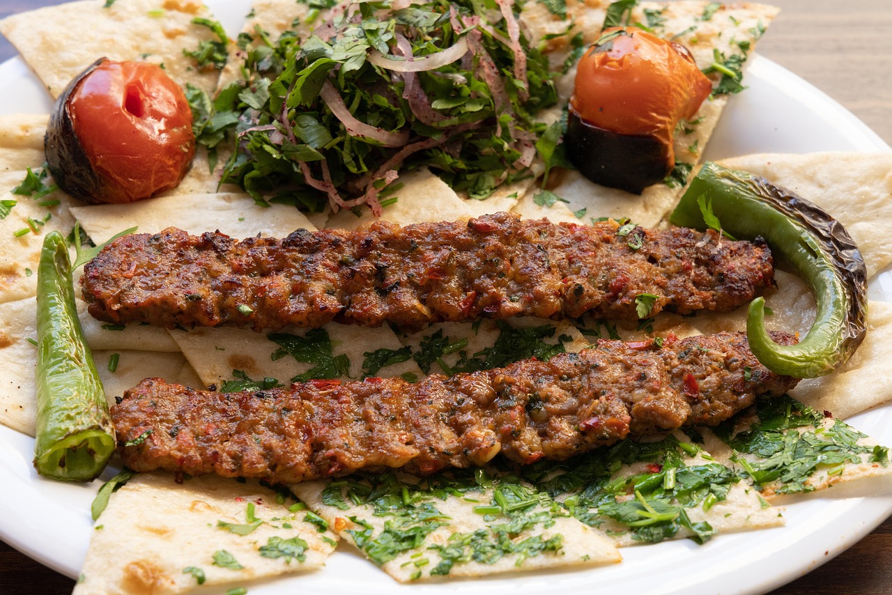 Spicy Adana kebab skewers served on flatbread with grilled tomatoes and green peppers.