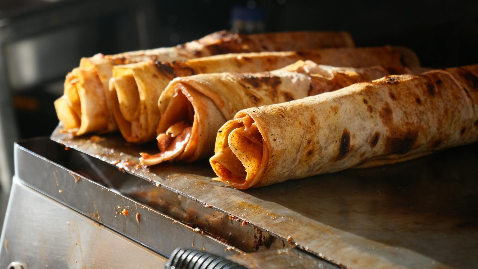 Freshly prepared spicy Mersin style tantuni wraps heating on a traditional metal cooking surface.