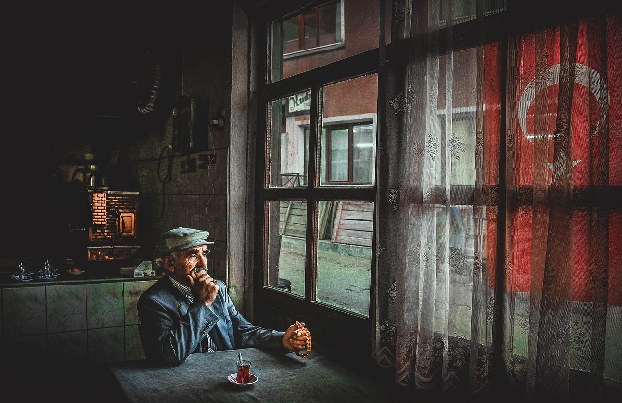 An elderly man sits at a table inside a traditional Turkish cafe with tea.