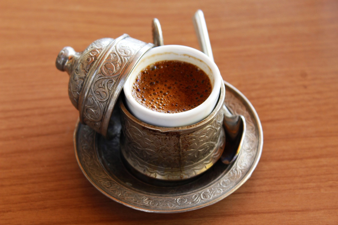 Frothy Turkish coffee served in a traditional ornate metal cup on a wooden table.