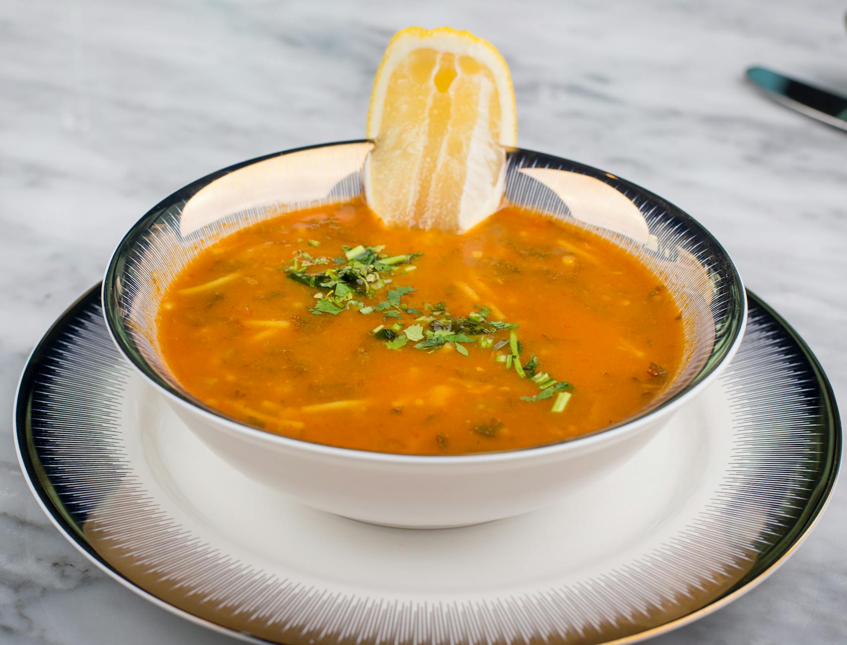 A bowl of traditional Turkish lentil soup garnished with fresh herbs and a lemon wedge.
