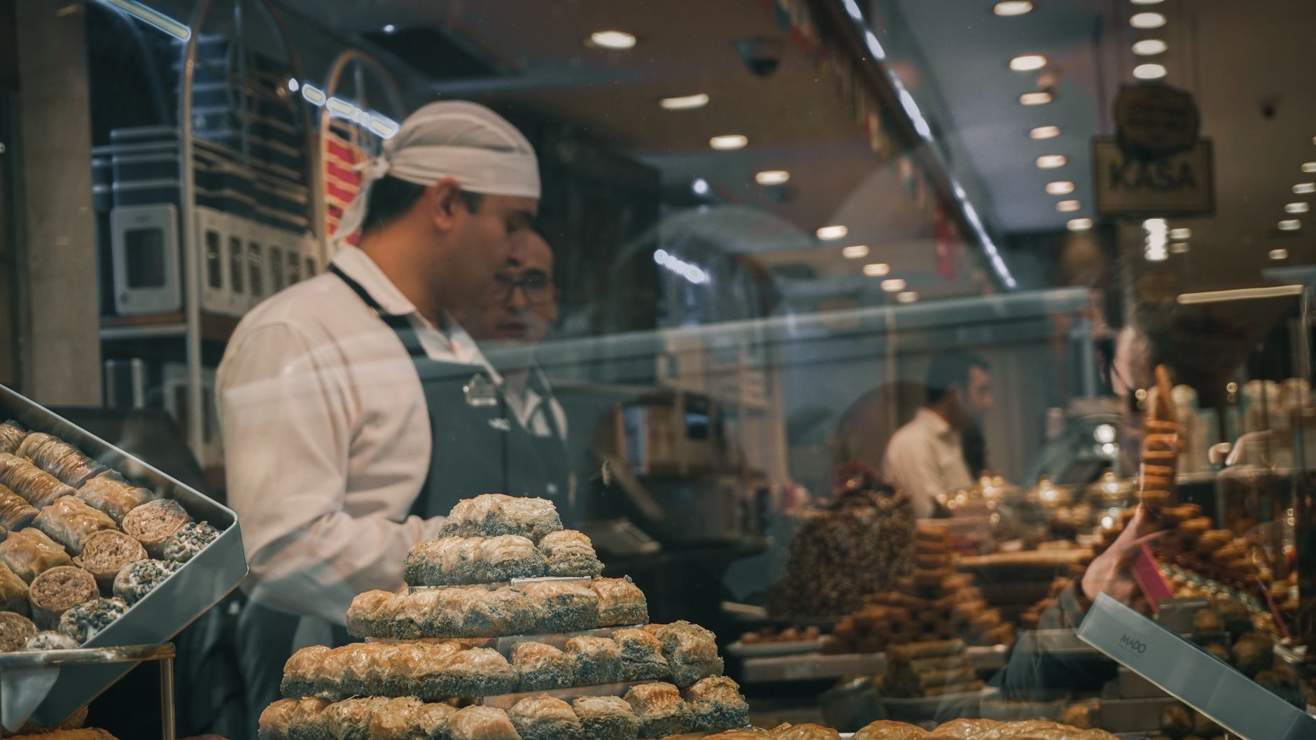 A Turkish baker serves fresh pistachio baklava inside a traditional pastry shop display.