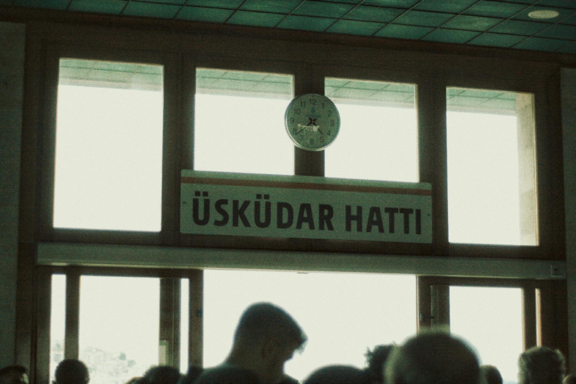 An indoor sign for the Uskudar ferry line above a crowd of commuters.