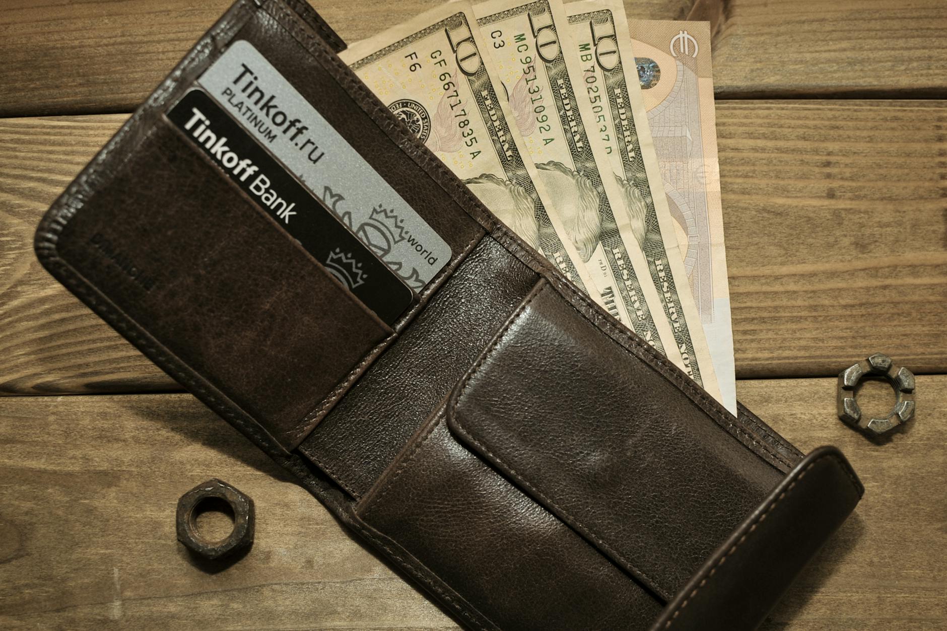 An open leather wallet filled with US dollars, euros, and several payment cards.