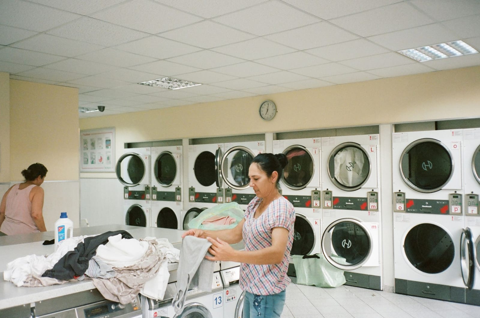 A woman folds clean laundry at a table inside a busy public laundromat.
