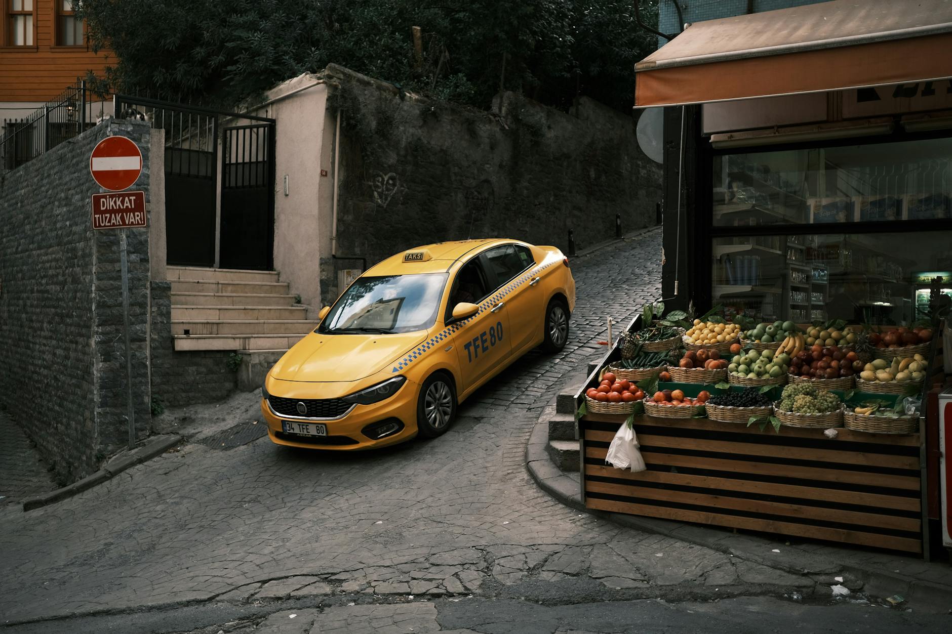 A yellow taxi carefully maneuvers down a steep and narrow cobblestone street in Istanbul.